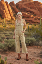 Beige distressed denim overalls with western boho desert background