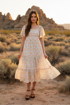 Cream floral print tiered midi dress with flutter sleeves and desert landscape