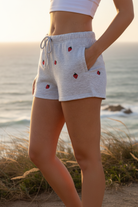 Grey shorts with strawberry embroidery and coastal cliff background - closer view