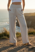 Light grey wide leg pants with smocked waistband and coastal cliff background