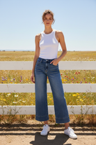 Medium wash wide leg cuffed jeans with white tank top in bright boho western setting