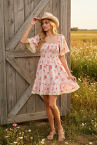 Pink floral smocked bodice mini dress with rustic barn wildflower meadow background