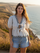 White and black striped embroidered top with tie front detail and denim shorts with coastal cliff background