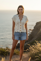 White crochet knit cardigan with wooden buttons and denim shorts with coastal cliff background